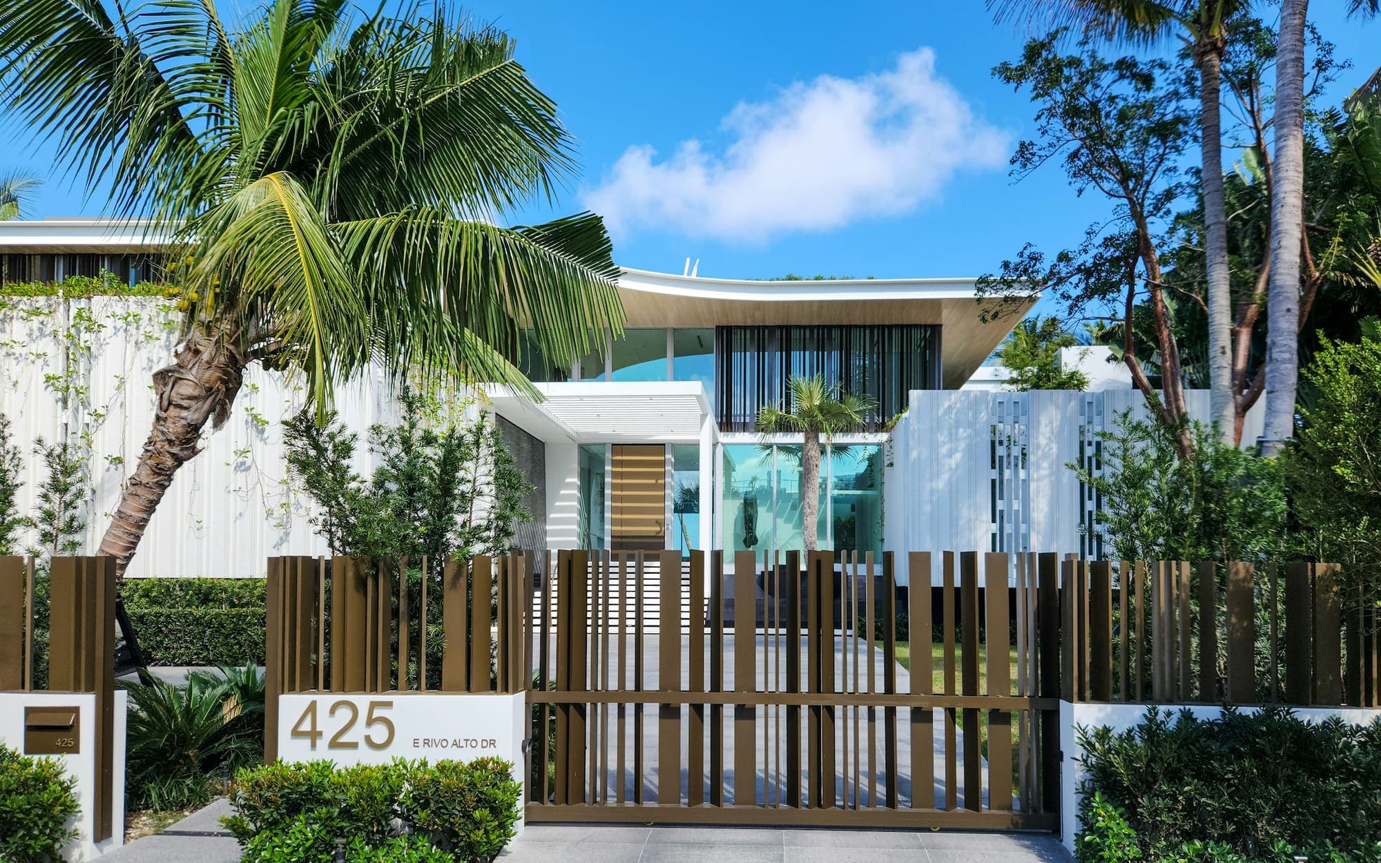 Modern white home with palms behind a wood slat gate
