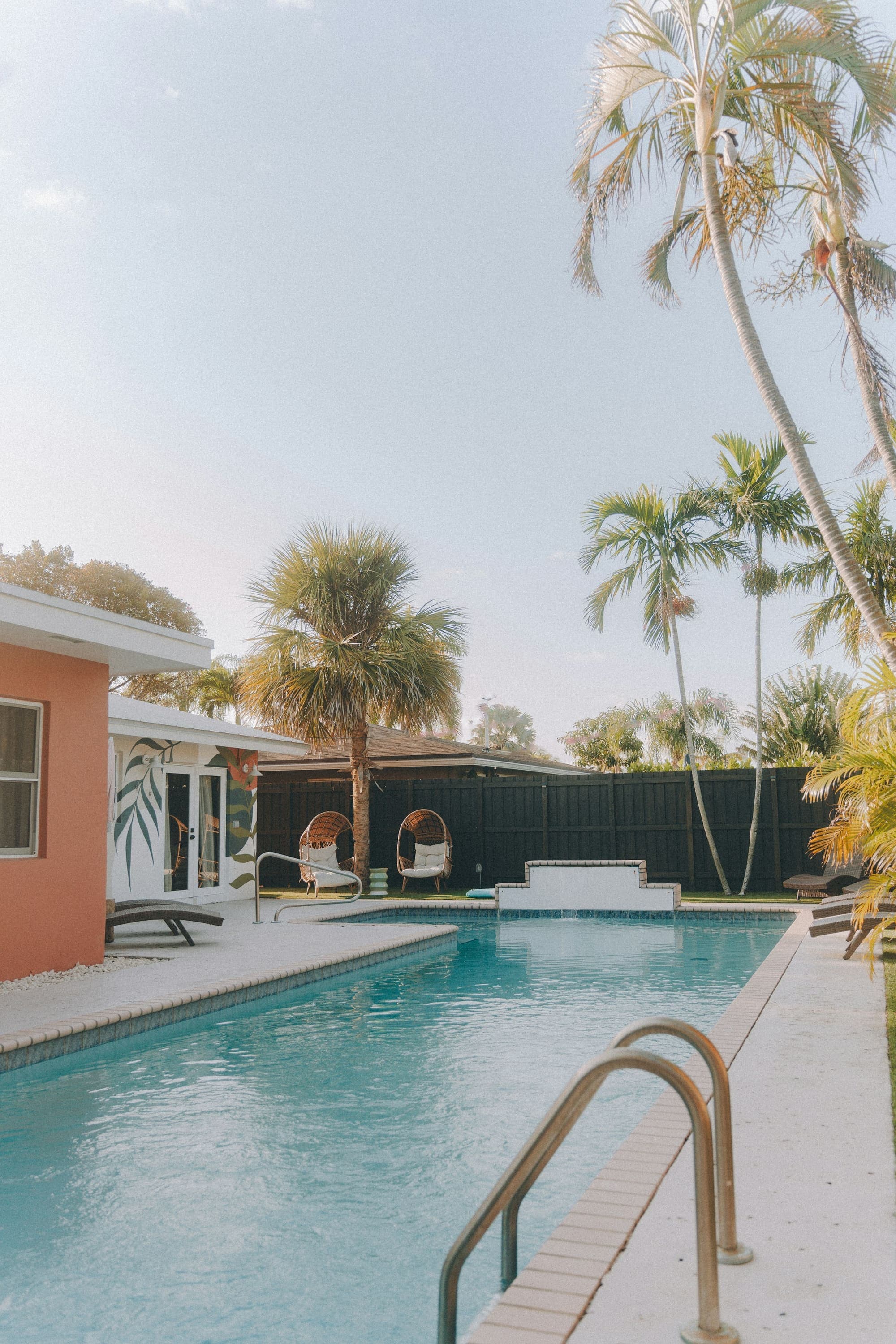 Pool beside a coral stucco house with palms and lounge chairs