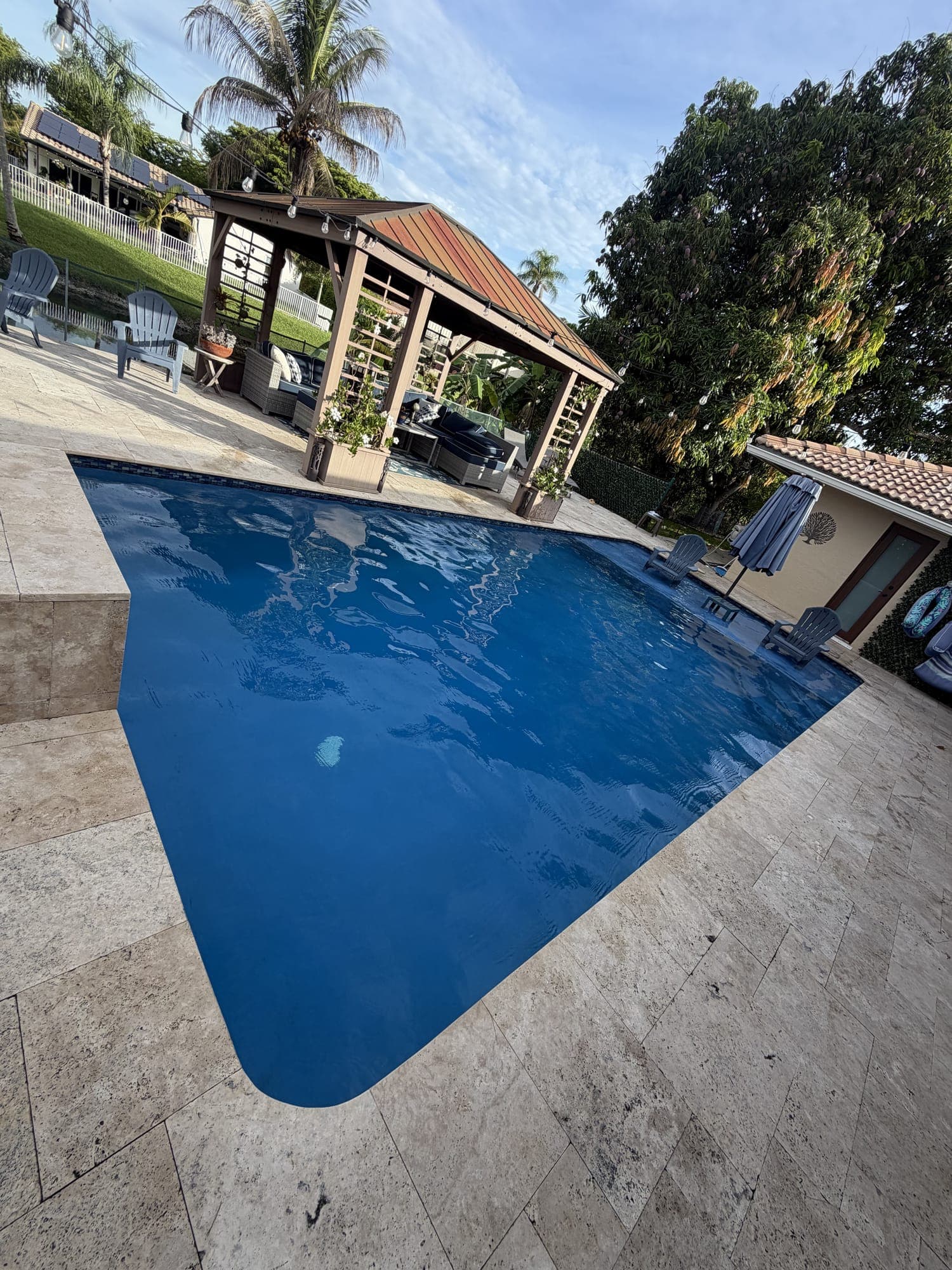 Deep blue pool with a travertine deck and a wood gazebo