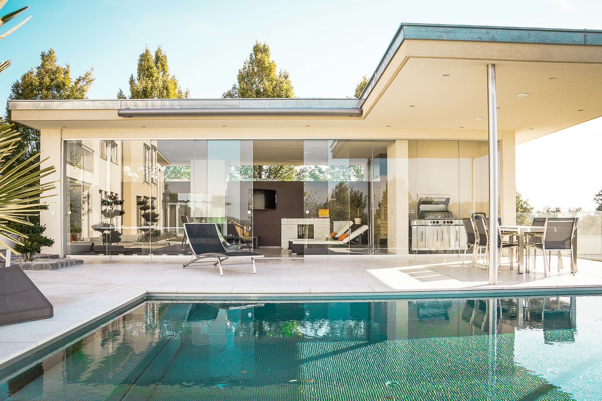Glass-walled modern home behind a long, still backyard pool